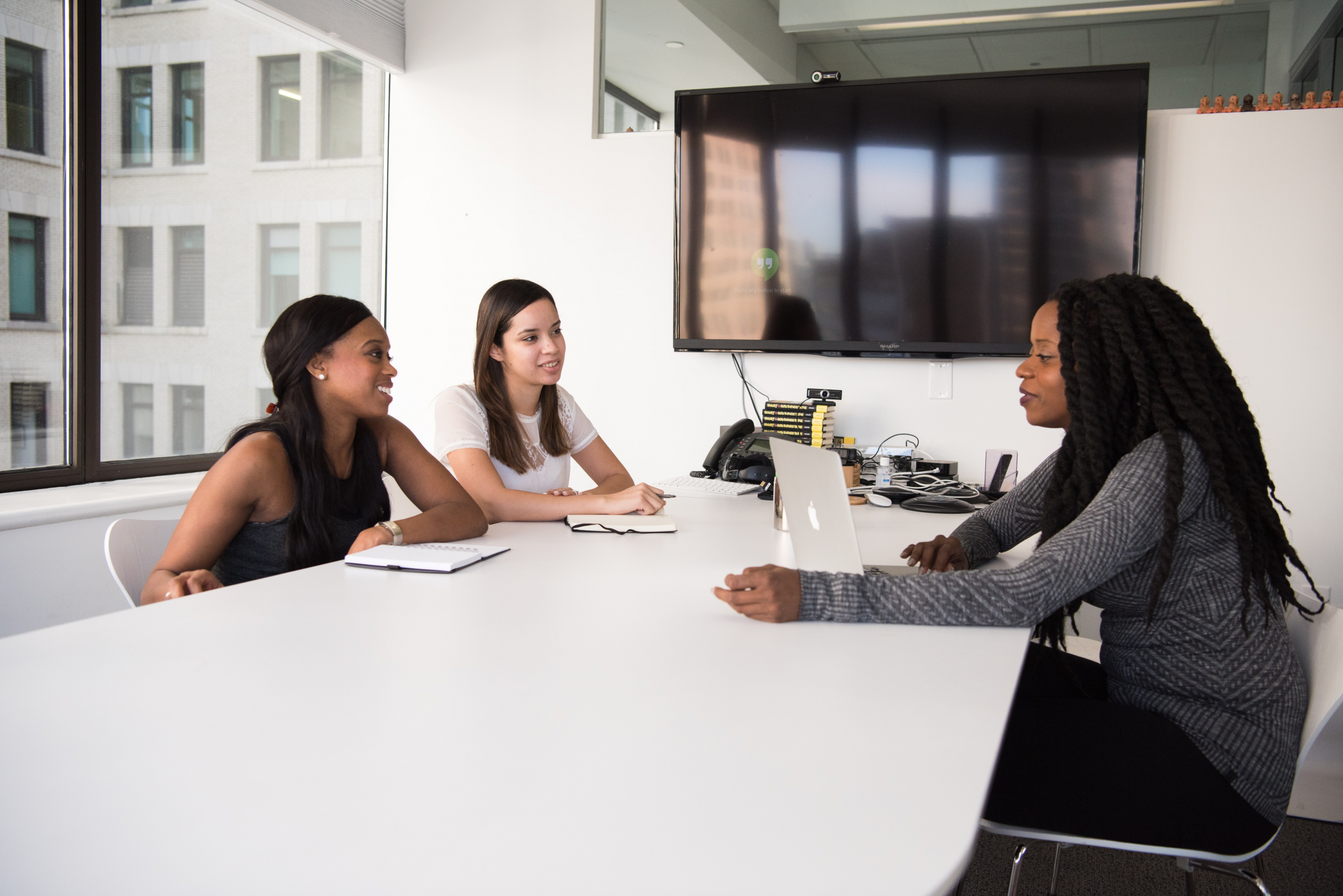 Picture of three women sitting around a white desk in a business setting