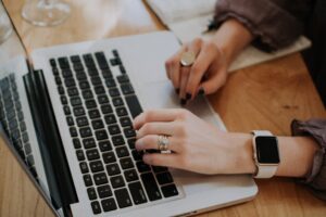 Hands of a woman typing on her laptop with an apple watch and multiple eclectic rings on her finger